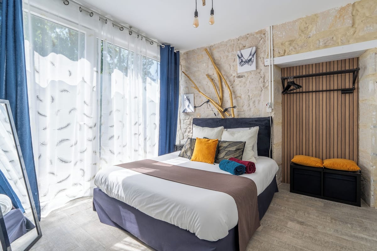 A hotel room with a large bed, a wooden headboard, a window with curtains, and a wall-mounted towel rack.