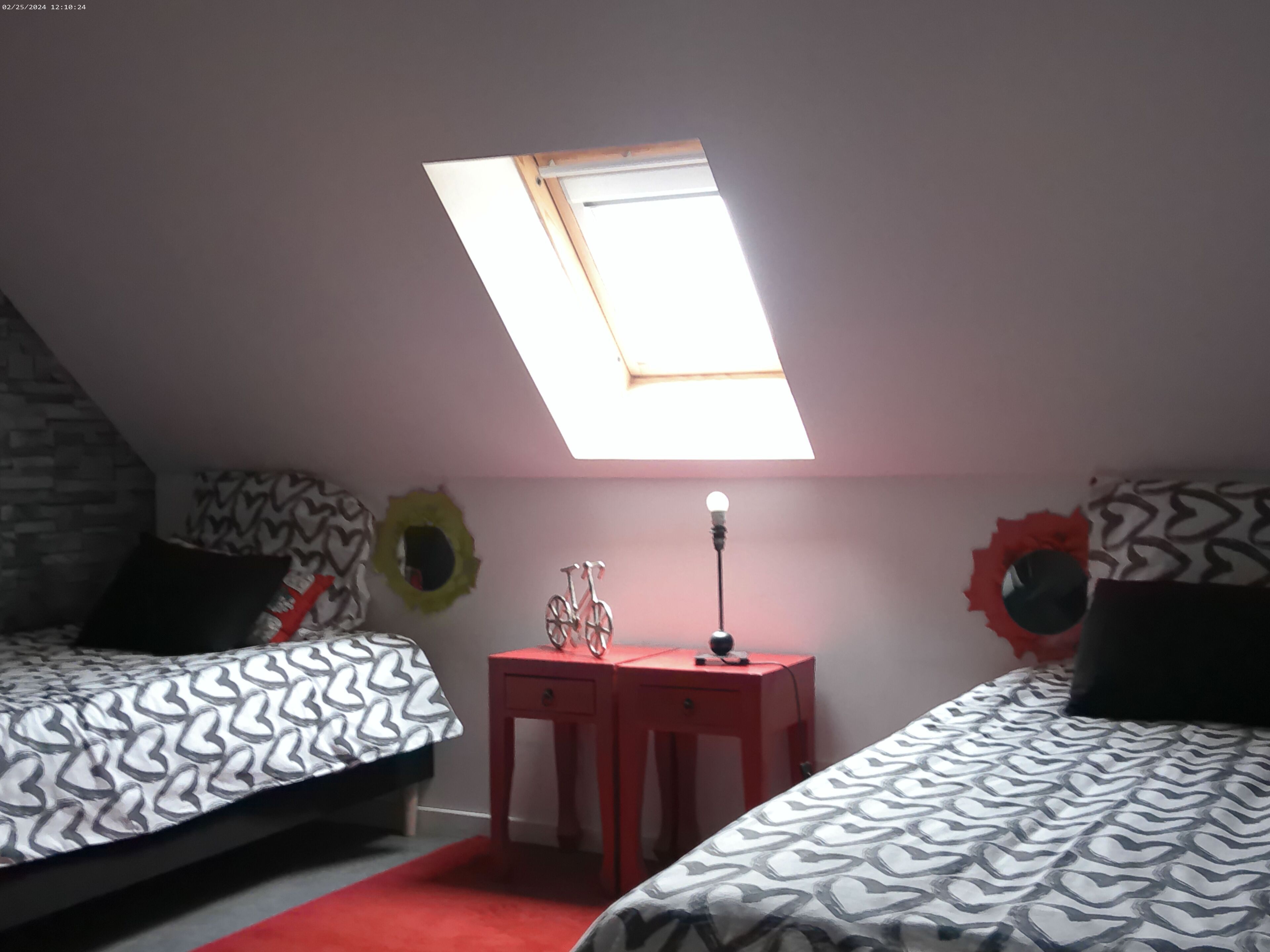 A bedroom with two beds, a skylight, a red nightstand, and decorative wall elements.