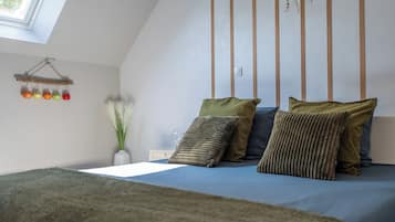 A bedroom with a sloped ceiling, a bed with multiple pillows, a bedside table with a lamp, and a wall-mounted shelf with jars.