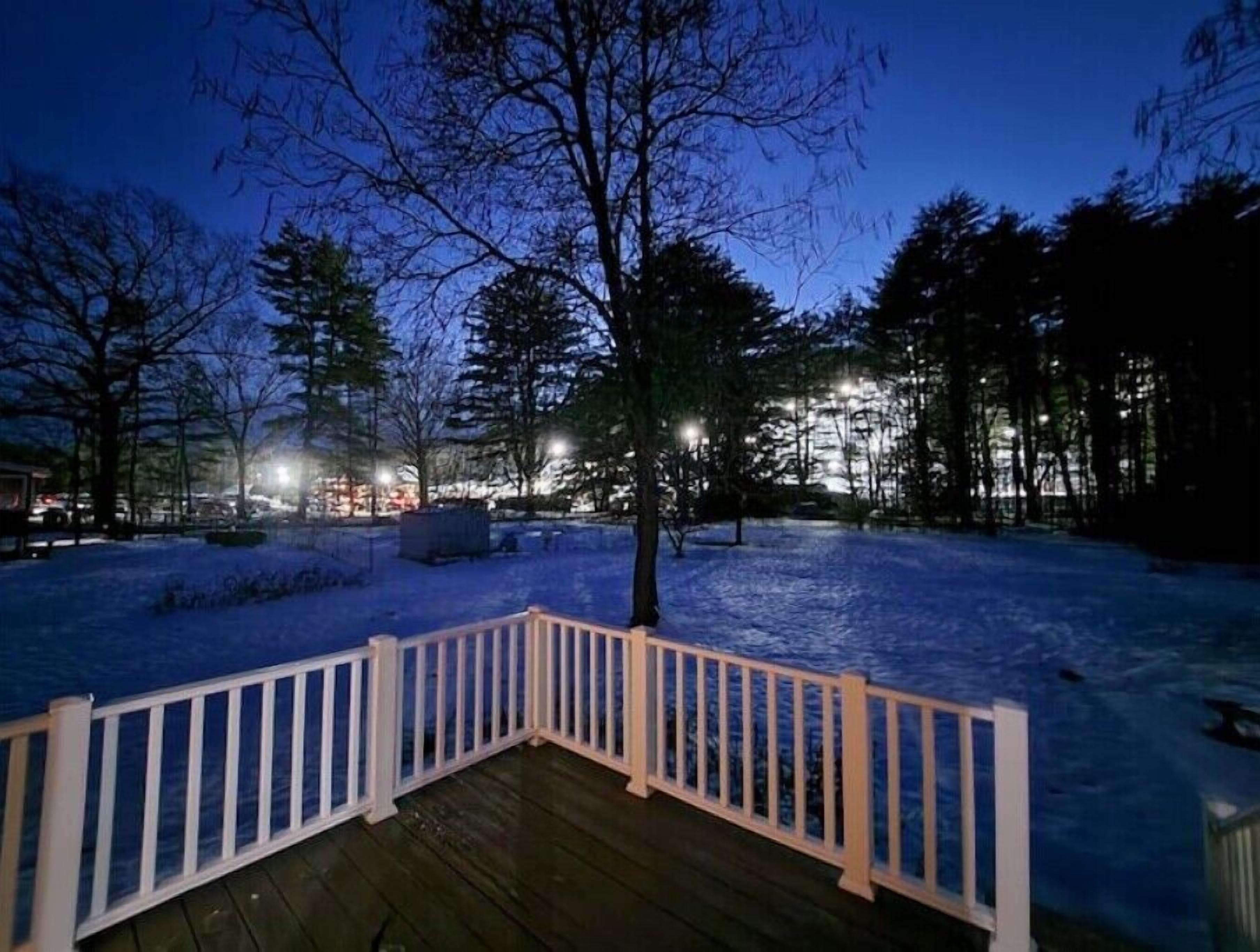 A wooden deck with a white railing, surrounded by snow-covered ground and trees.