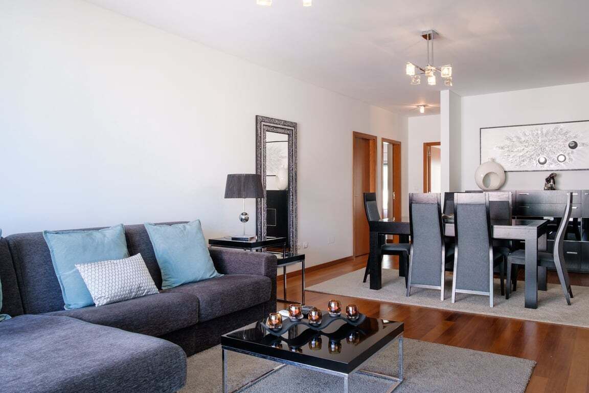 Un salon moderne avec un canapé gris, une table basse et un coin repas comprenant des chaises et une table.
