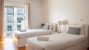 A hotel room with two beds, a balcony, and a view of buildings.