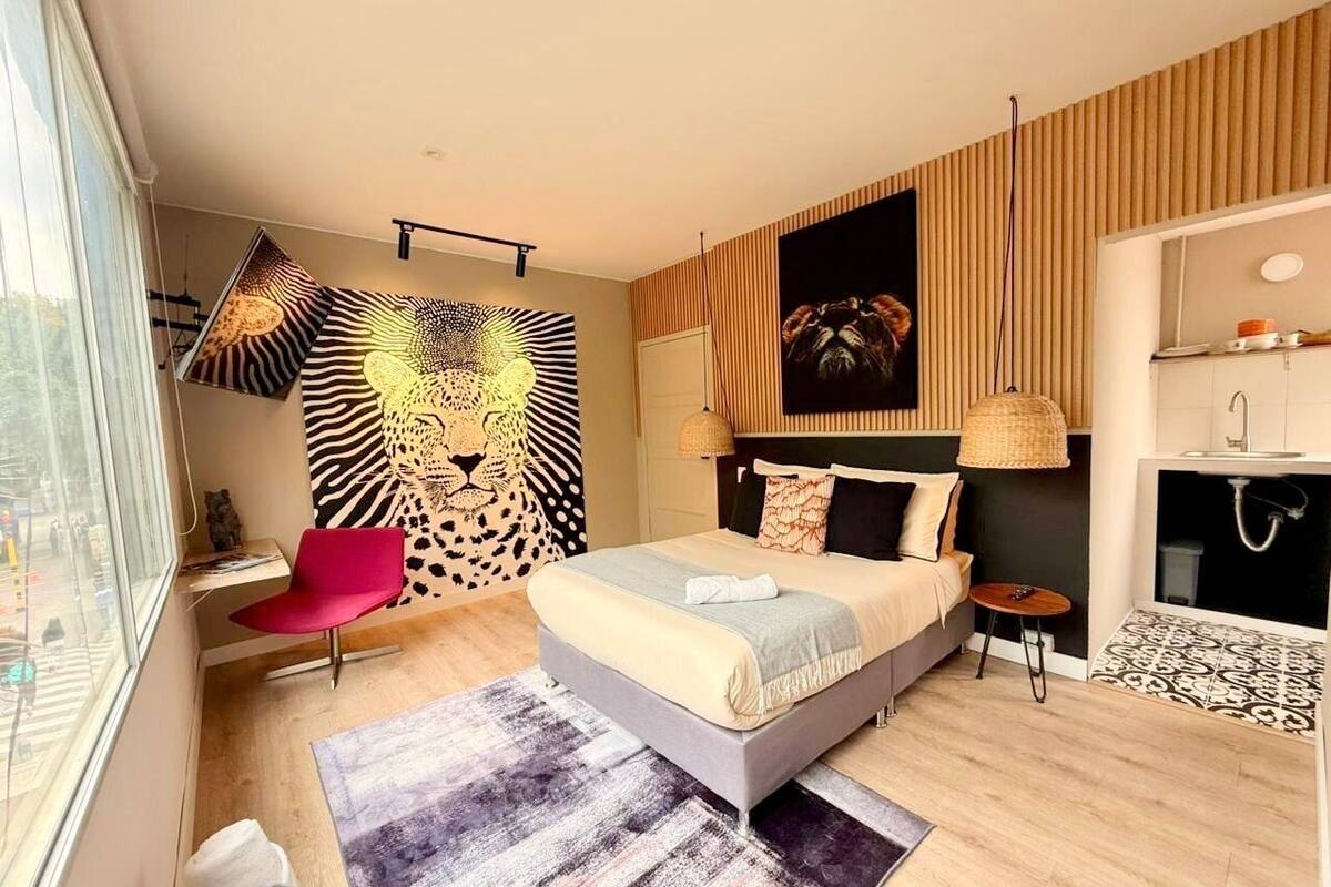 A modern bedroom with a bed, a chair, a large wall mural, a hanging lamp, and a small table.