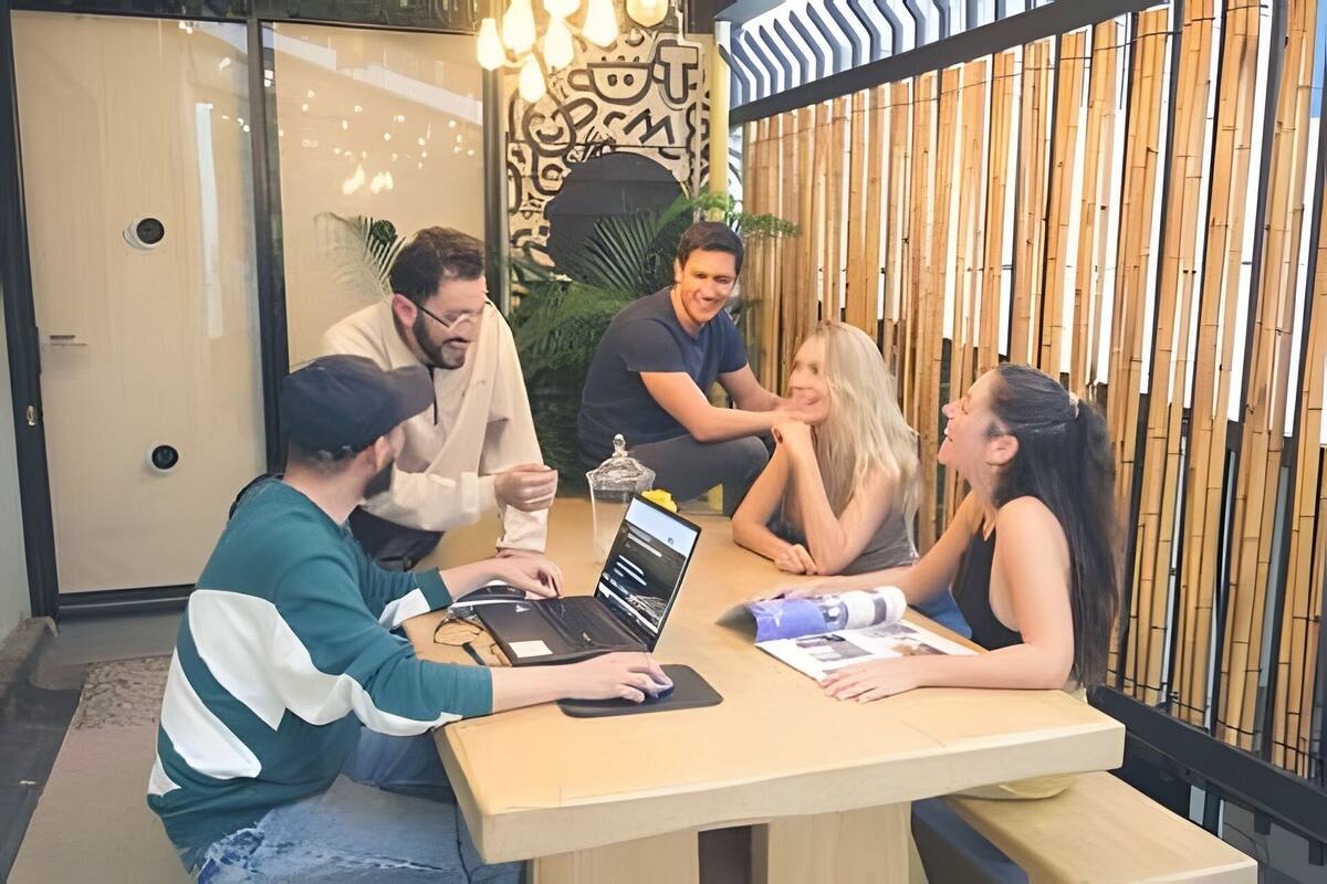 A group of people in a meeting room with a laptop, papers, and a decorative wall.