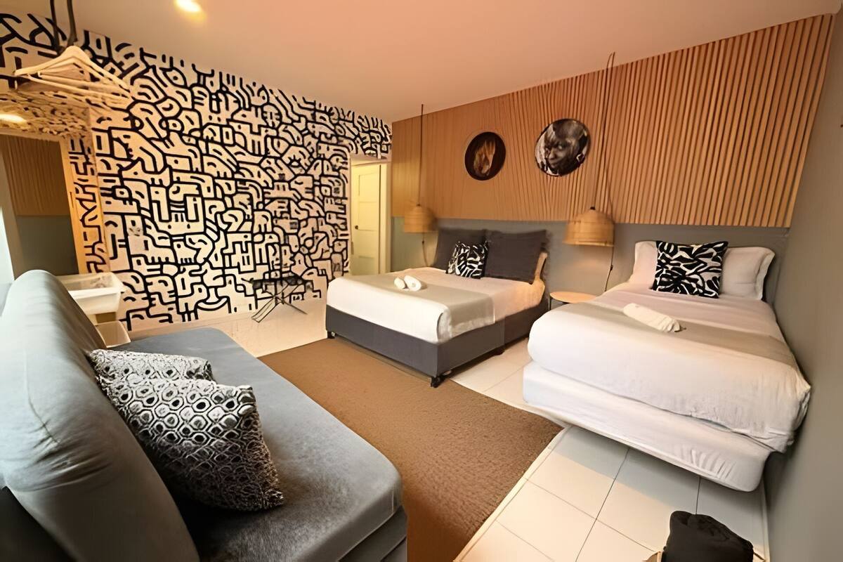 A hotel room with two beds, a sofa, a patterned wall, and a wooden panel wall.