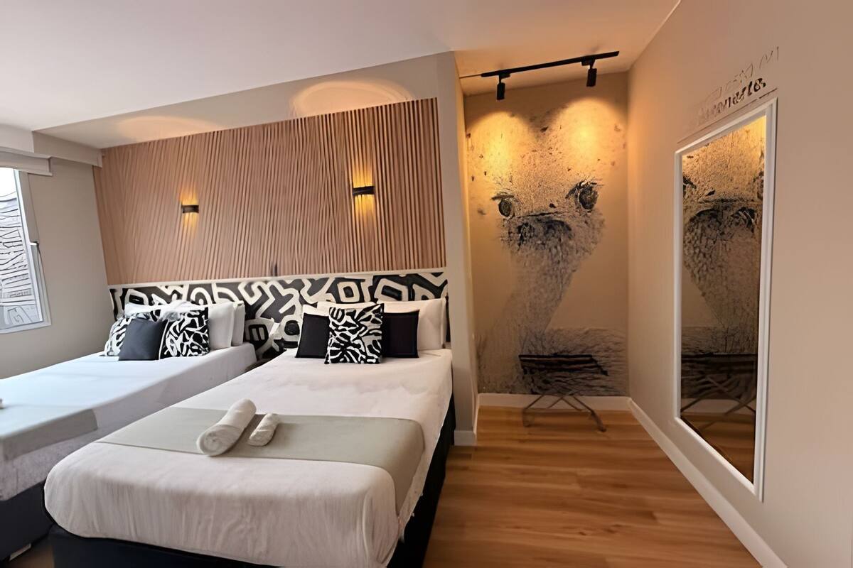 A modern hotel room with two beds, a wooden slat wall, a large abstract painting, and a view of the city.