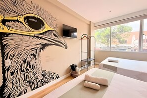 A hotel room with a large wall mural, a TV, a metal rack, and two beds. - Nomadia Hostel (Bogotá)
