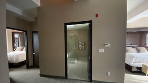 A hotel room with a large bed, a separate bathroom, and a glass door leading to a hallway.