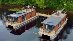 A floating houseboat with a deck, windows, and a small outdoor seating area.