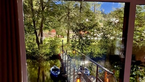 A view through a window of a wooden bridge over a body of water, with trees and a building in the background.