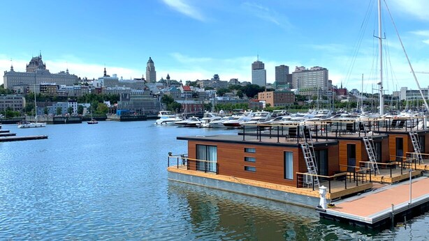 A floating structure with a wooden deck and metal railings, docked in a marina with several boats. - Marina Port de Québec 1 - Maison flottante (Québec City)