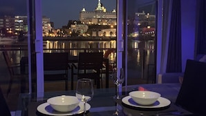 A dining table with two bowls and wine glasses, overlooking a cityscape with illuminated buildings at night.