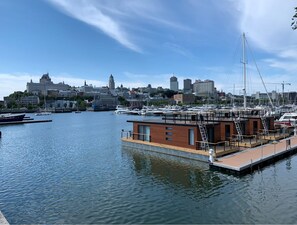 A marina with boats docked, a modern building with wooden siding, and a cityscape in the background.