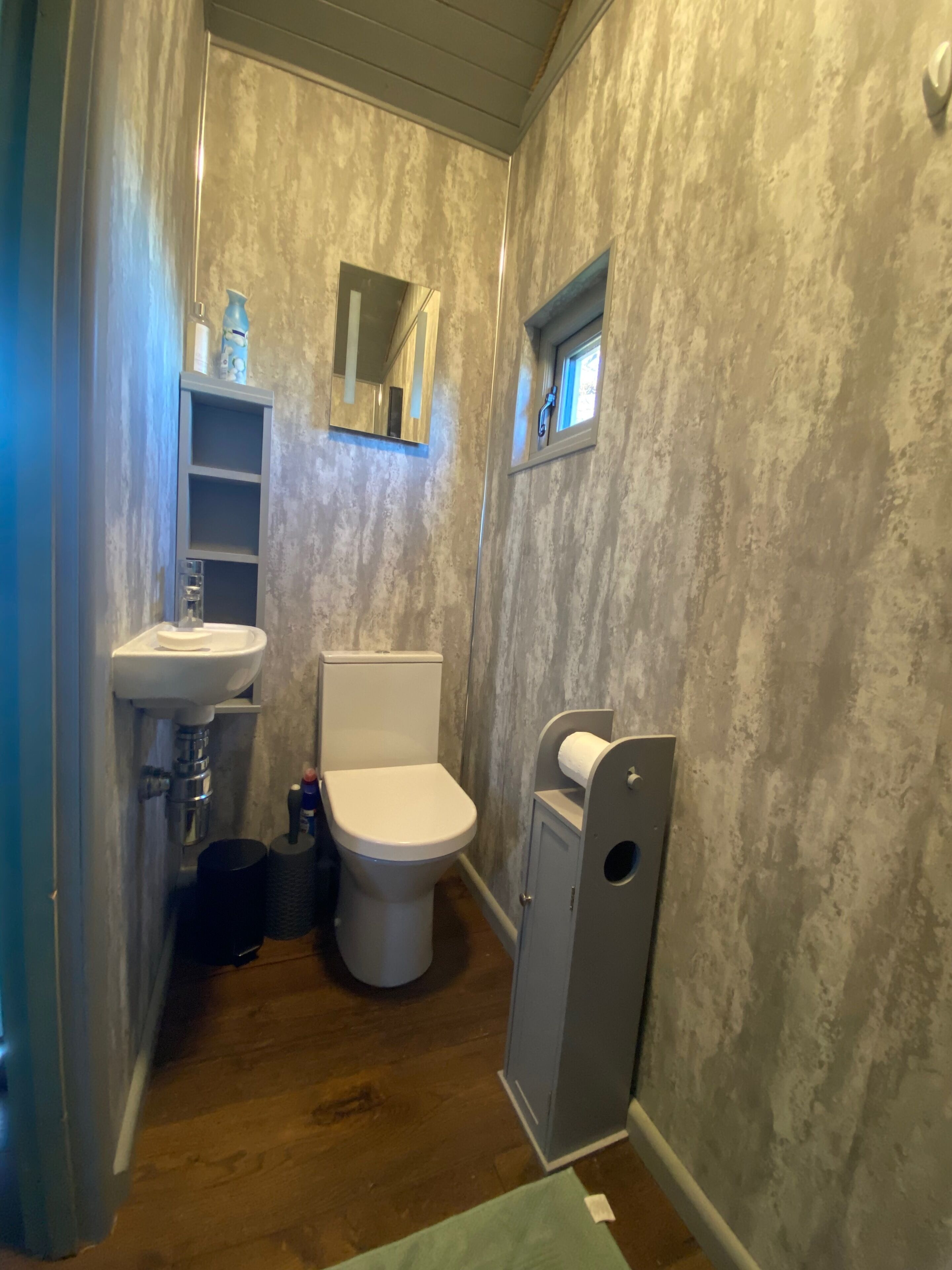 Et badeværelse med toilet, vask og et lille vindue.