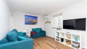 Ein modernes Wohnzimmer mit zwei smaragdgrünen Sofas, einem Flachbildfernseher und einem Stadtbild an der Wand.