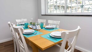 Ein Esstisch ist mit weißen Tellern, blauem Glas und platzfarbenen Unterlagen in einem Raum mit weißen Wänden und einem Fenster mit Gitterwerk gedeckt.