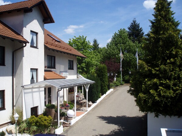 A two-story building with a sign reading "Gästehaus" on the facade, a covered outdoor seating area with tables and chairs, and a paved driveway leading to the entrance. - Schweizerhof (Böbingen an der Rems)