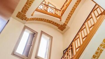 Un interior de varios niveles con una escalera de madera, patrones decorativos en las paredes y ventanas.