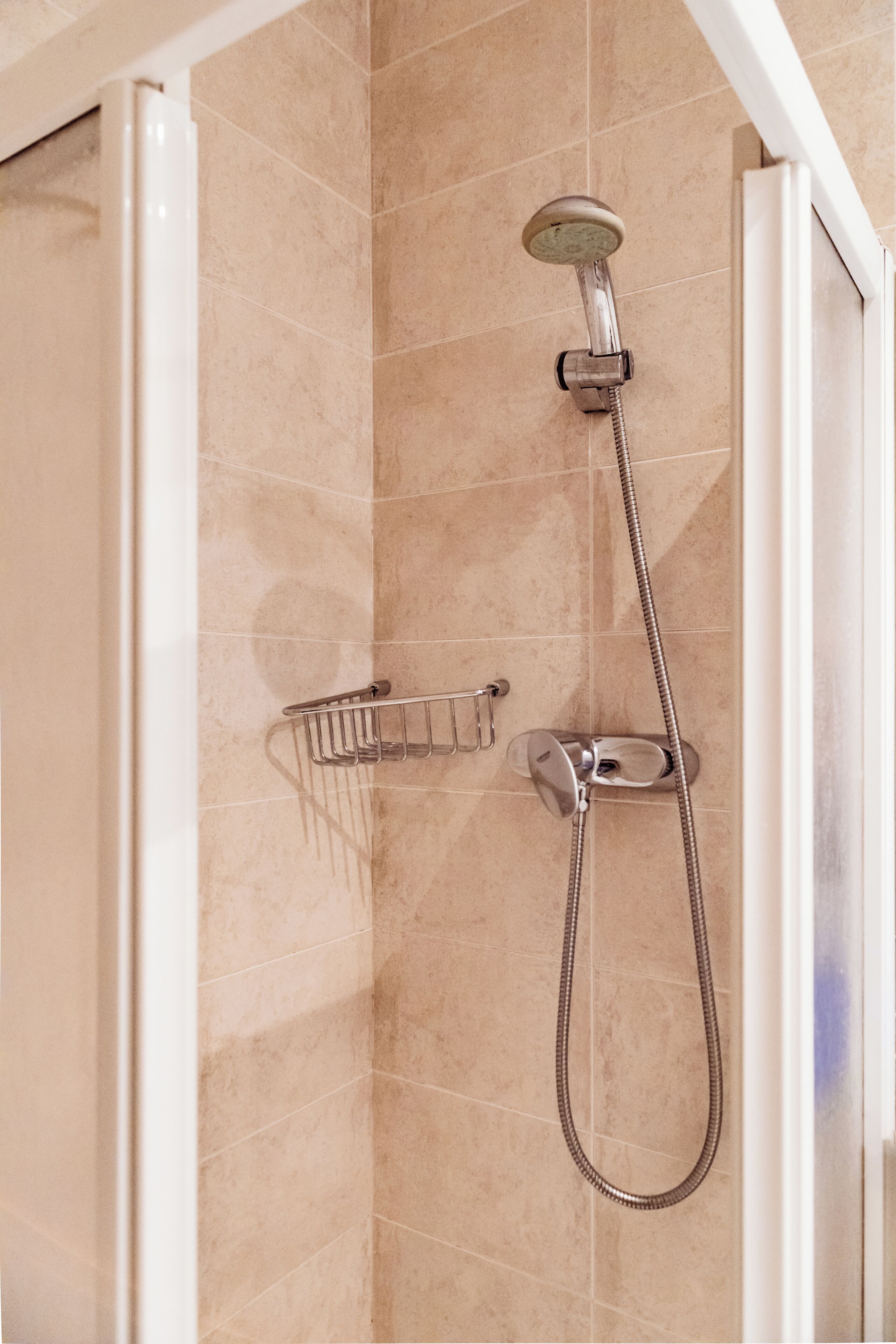 A shower with a handheld showerhead and a wall-mounted faucet, a towel rack, and a shower control panel.