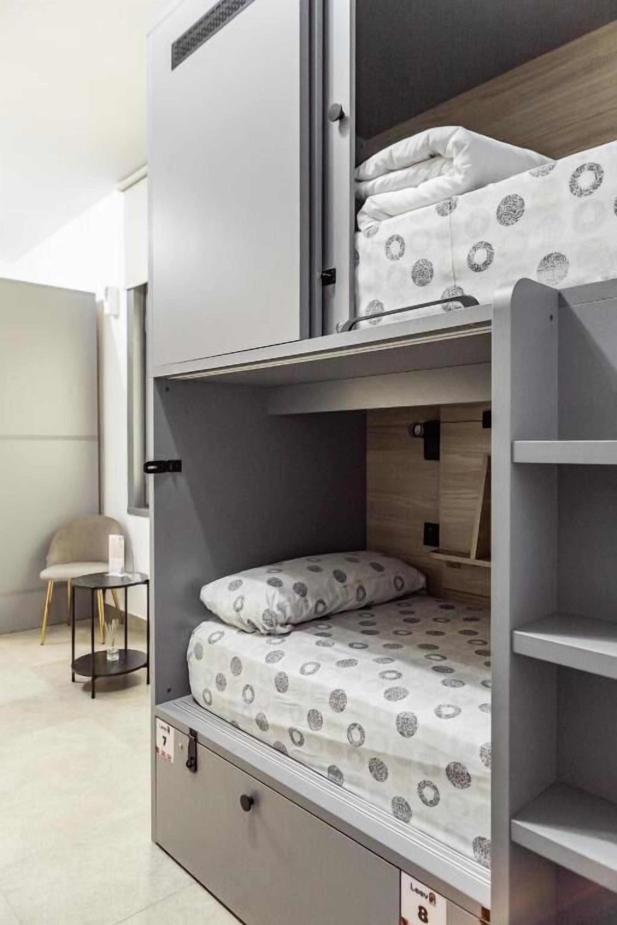 Una cama litera con una cama inferior, una mesita pequeña y una silla en una habitación con suelo de baldosas.