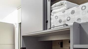 Una cama litera con una cama inferior, una mesita pequeña y una silla en una habitación con suelo de baldosas.