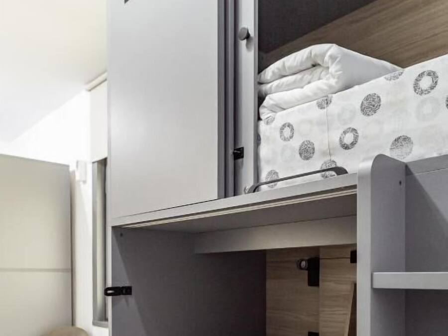 Una cama litera con una cama inferior, una mesita pequeña y una silla en una habitación con suelo de baldosas.