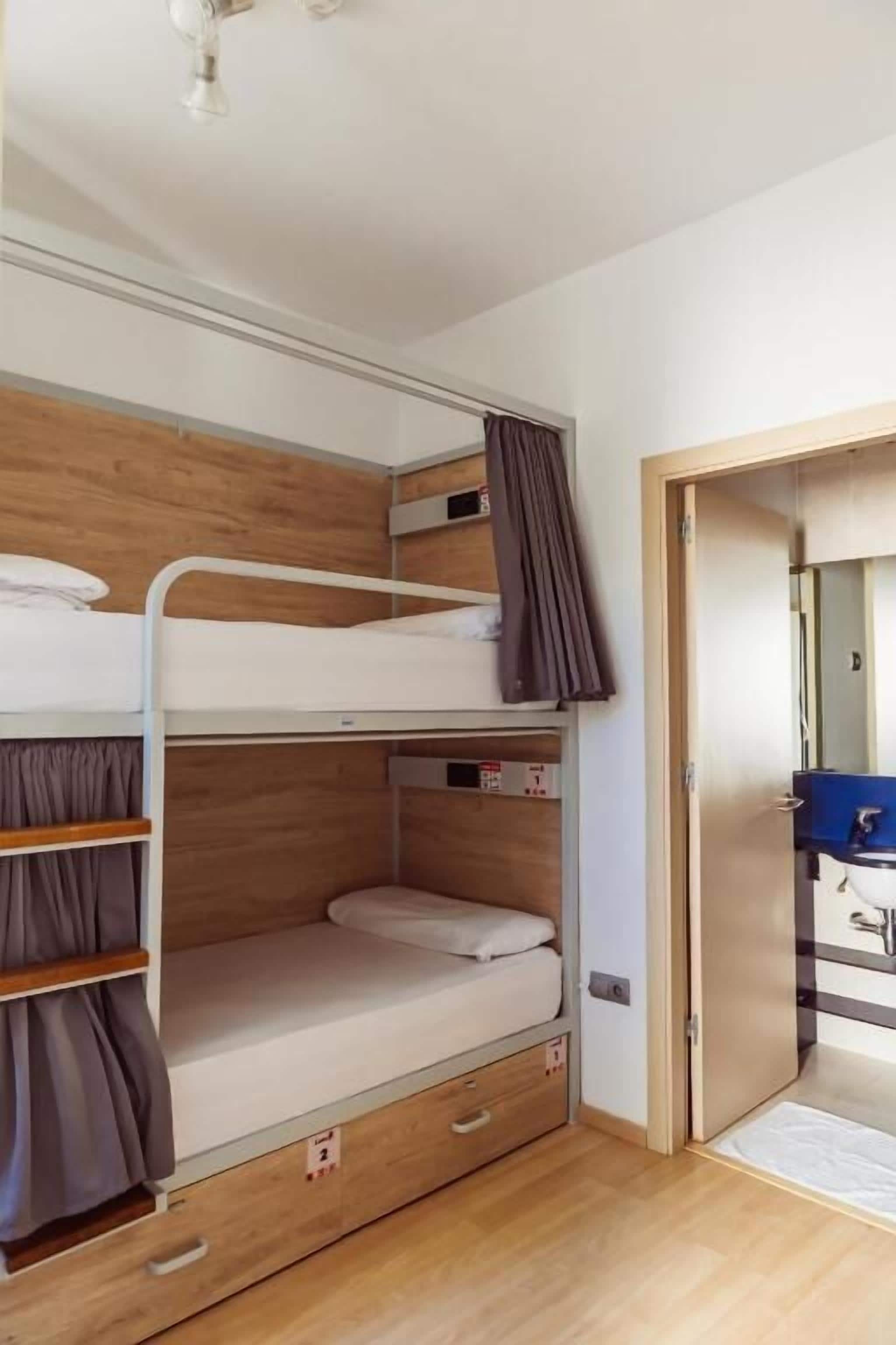 Habitación con literas, piso de madera, un escritorio pequeño y un baño con un lavabo azul.
