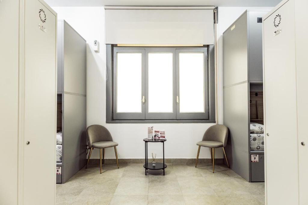 Una habitación pequeña con un ventanal grande, dos sillas, una mesita y un armario.