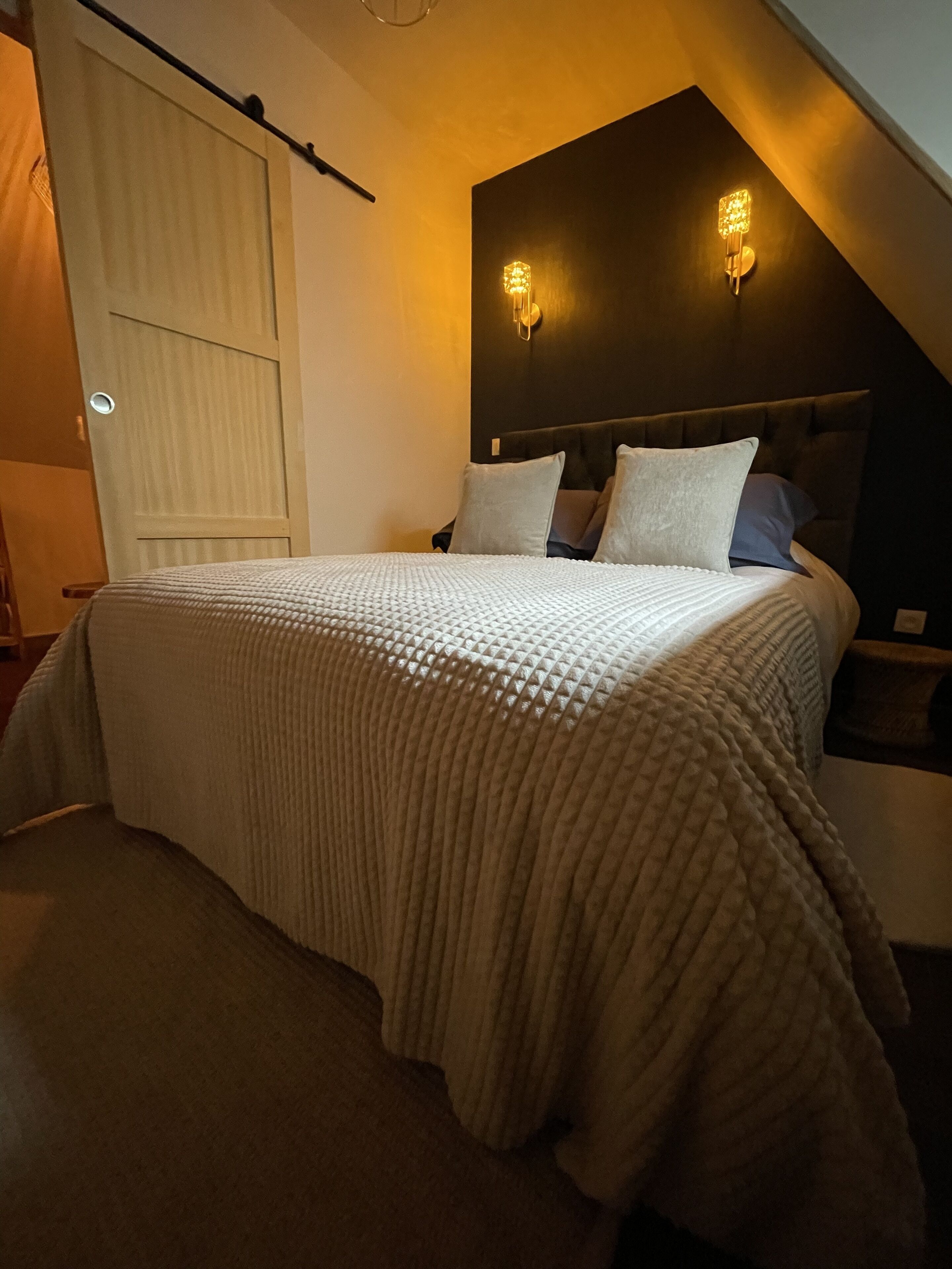 Une chambre à coucher avec un grand lit, une tête de lit dotée de lampes fixées au mur et une porte coulissante.