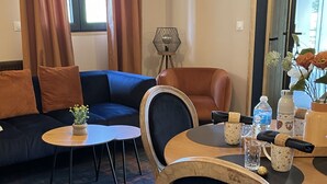 Una sala de estar moderna con un sofá azul, un sillón de cuero marrón, una mesa de comedor de madera y una mesita auxiliar con una planta.