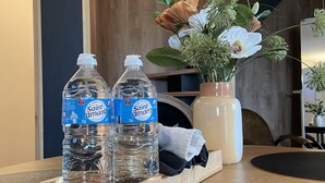 Una mesa de madera con dos botellas de Saint Amard, una toalla doblada y un florero con flores.