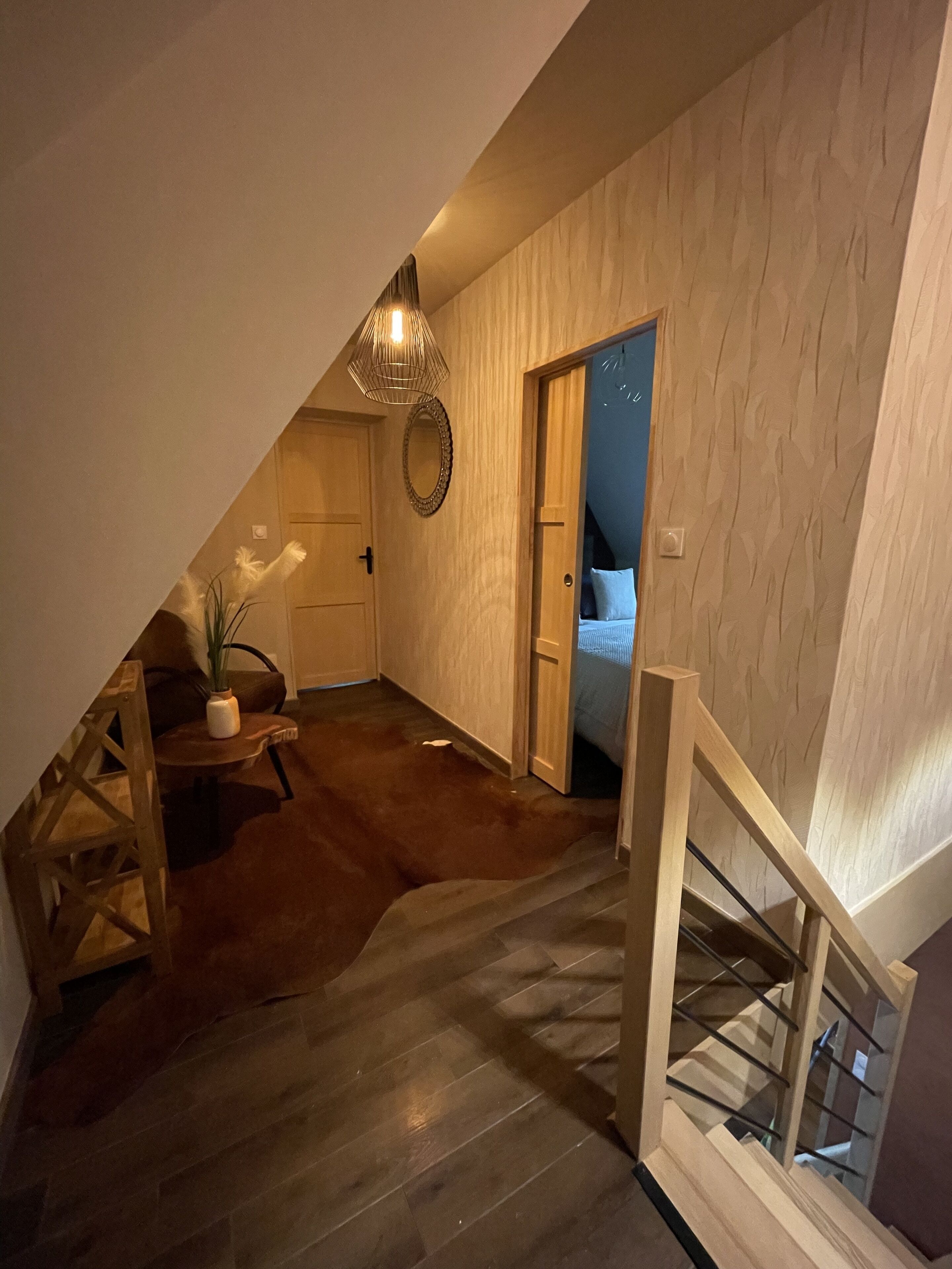 Un dormitorio acogedor en el ático, con techo inclinado, una escalera de madera y vista al cielo nocturno a través de una puerta abierta.