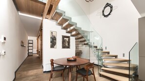A modern interior with a wooden staircase, a dining area with a round table and chairs, and framed pictures on the walls. - Historical Two-Bedroom Penthouse in the Centre - Kolkovna (Hlavní mesto Praha)