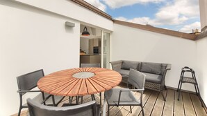 A patio with a round wooden table and chairs, a grey sofa, and a black ladder. - Historical Two-Bedroom Penthouse in the Centre - Kolkovna (Hlavní mesto Praha)