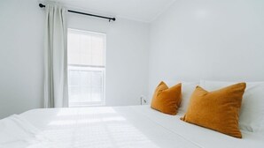 Ein Schlafzimmer mit einem großen Bett, weißer Bettwäsche und zwei orangen Kissen.