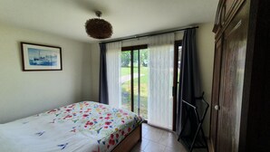 A bedroom with a bed, a framed picture on the wall, and a view of a garden through a sliding door.