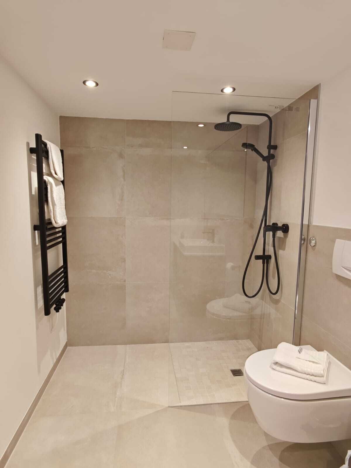 Un baño moderno con cabina de ducha de vidrio, un perchero negro y un inodoro blanco.