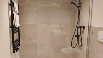 Un baño moderno con cabina de ducha de vidrio, un perchero negro y un inodoro blanco.