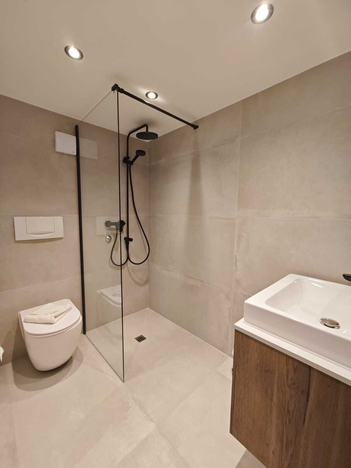 A modern bathroom with a glass-enclosed shower, a white toilet, and a wooden vanity with a sink.