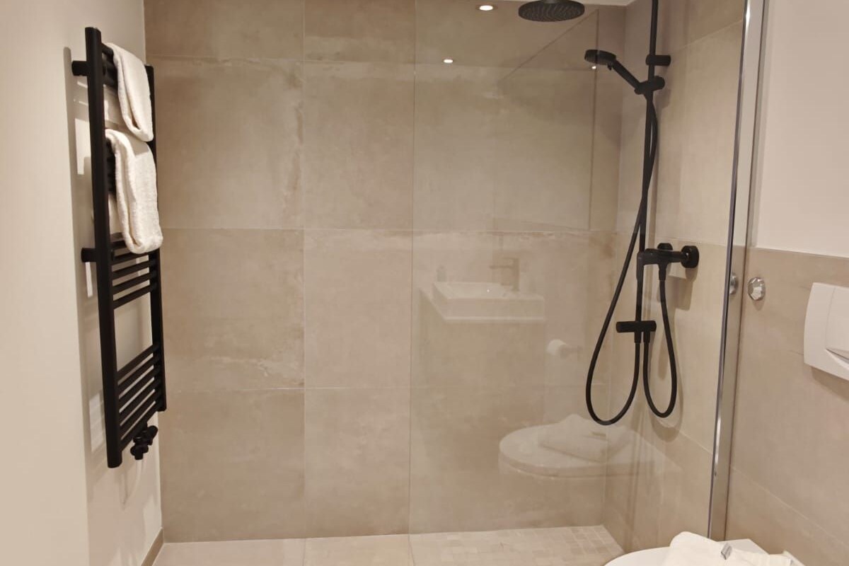 Een moderne badkamer met een douche met glazen wand, een zwarte handdoekhouder en een wit toilet.