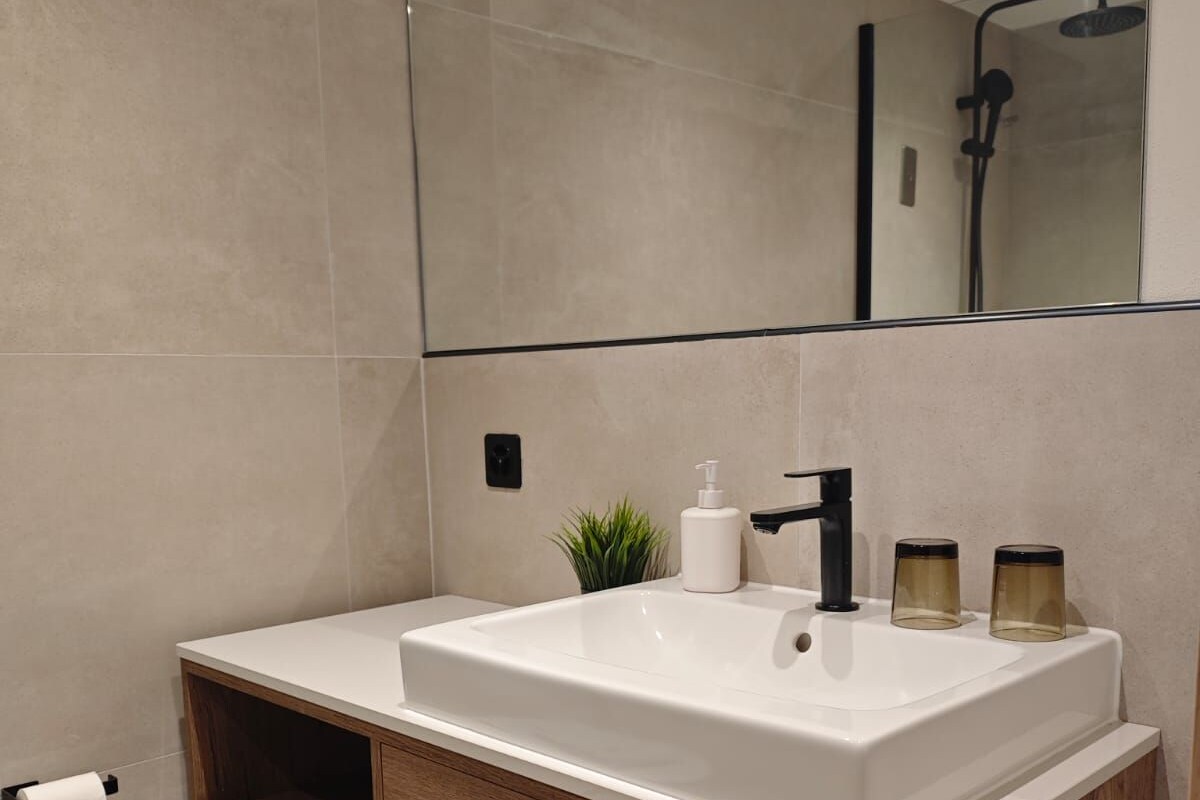 Een moderne badkamer met een groot wit wastafelmeubel, een houten opbergkast en een spiegel erboven.