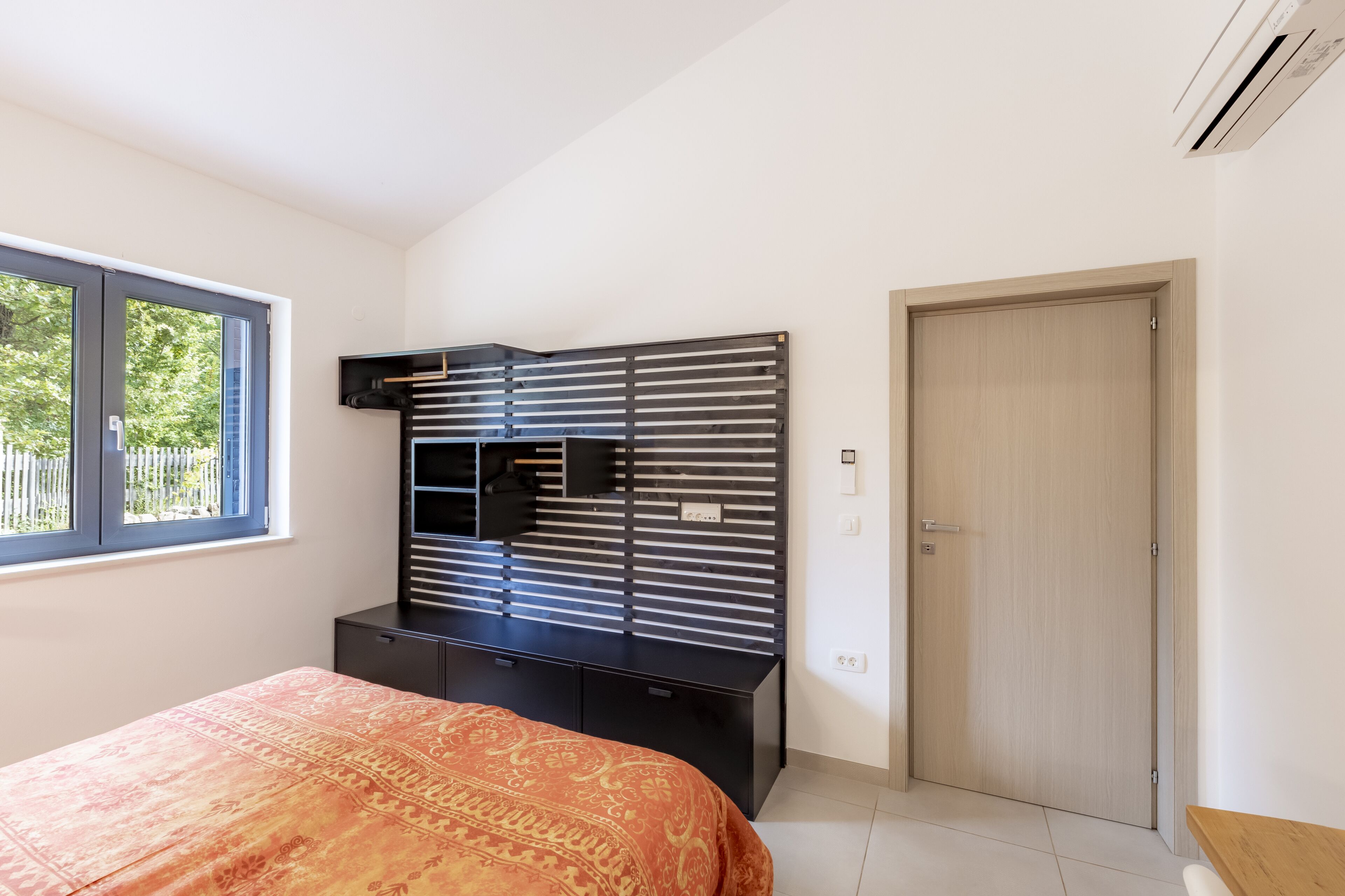 A bedroom with a bed, a black entertainment unit, a window, and a door.