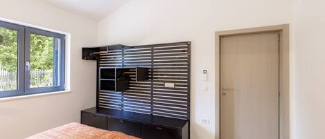 A bedroom with a bed, a black entertainment unit, a window, and a door.