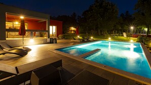 A modern outdoor pool area with lounge chairs, a bar, and a well-lit patio.