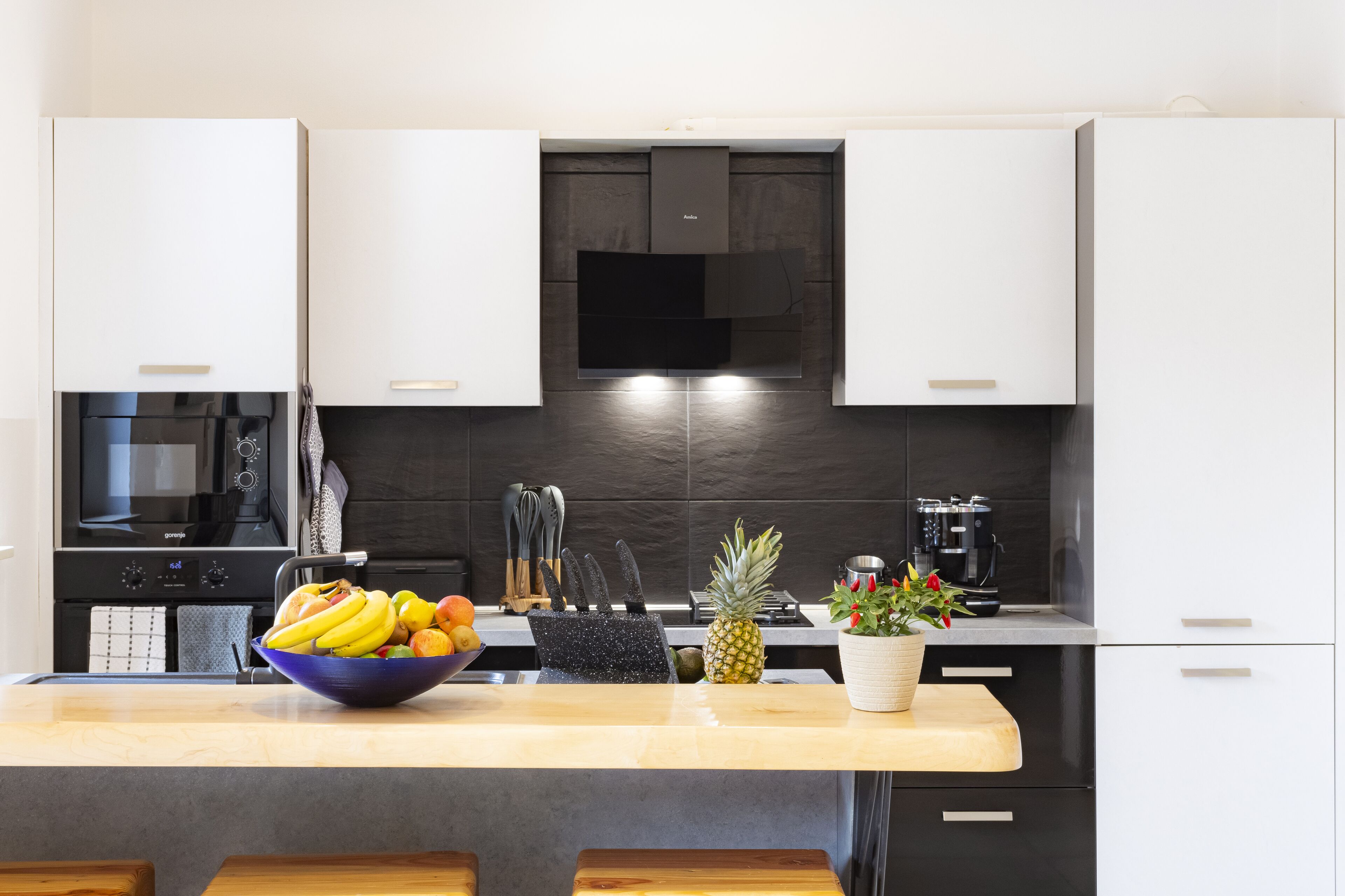 A modern kitchen with white cabinets, a black microwave, and a bowl of fruit on the counter.