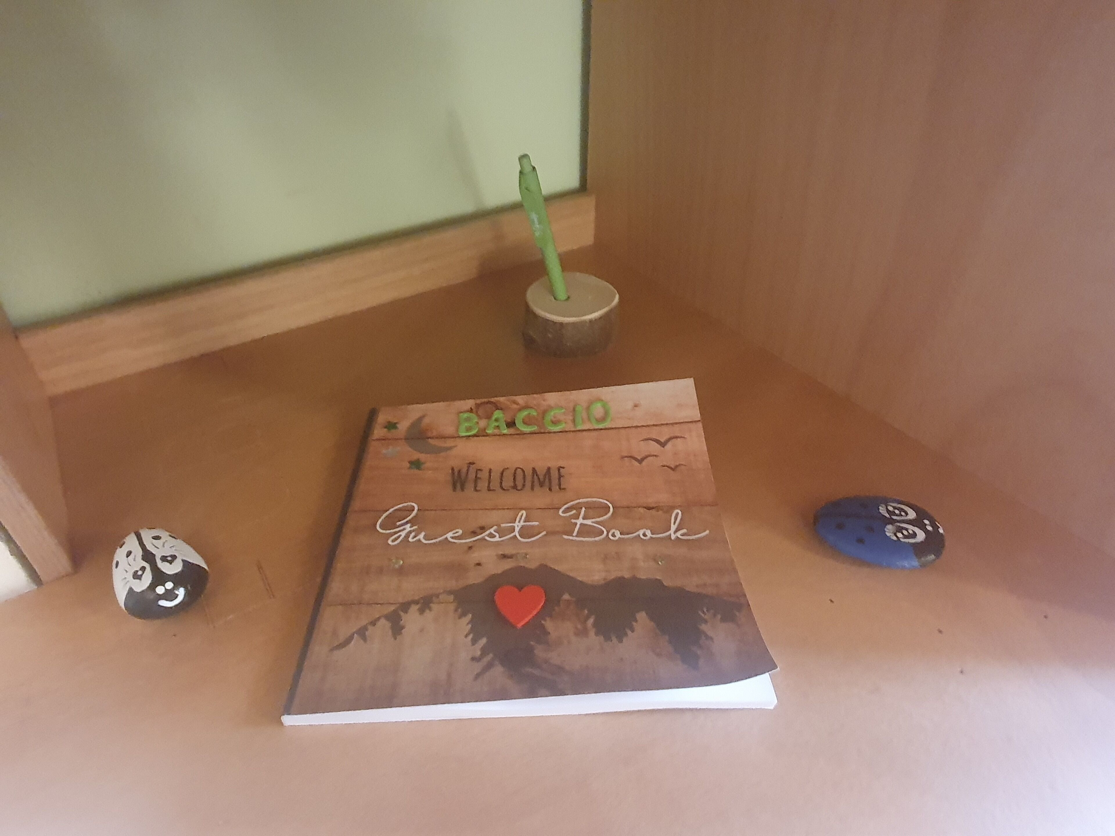 Una estantería de madera con un cartel de bienvenida, un libro de visitas y dos piedras decorativas.