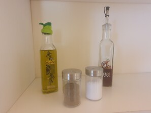 A shelf with a bottle of olive oil, two salt shakers, and a bottle with a chef illustration.