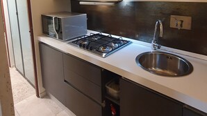 Una cocina moderna con estufa a gas, pileta de acero inoxidable y muebles blancos.