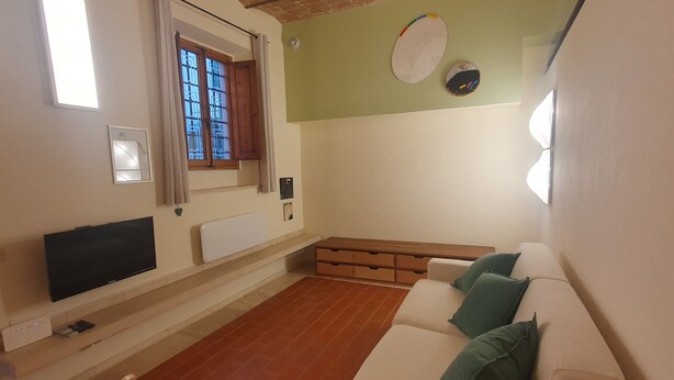 Un salón con un sofá blanco, un televisor de pantalla plana, una ventana con cortinas y una pared verde.
