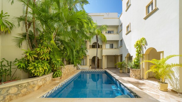 A swimming pool surrounded by lush greenery and a multi-story building with a tiled floor.